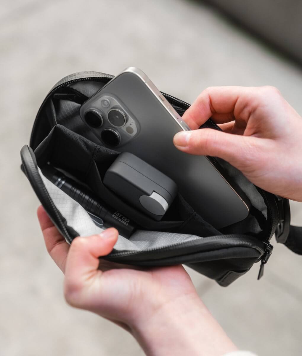 Woman sorting through items like an iPhone and earbuds while holding the Flight Pouch